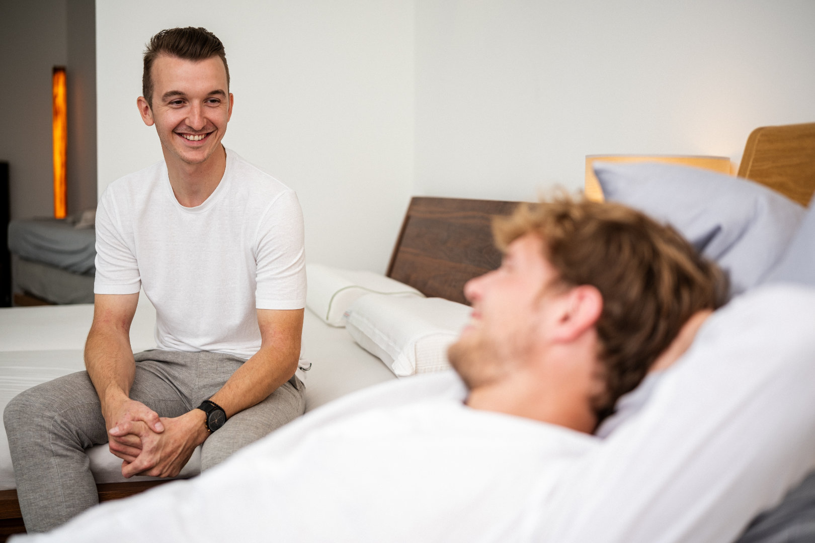 Berater von Betten VIKINGS spricht lächelnd mit einem Kunden, der entspannt im Bett liegt – persönliche Schlafberatung in Bielefeld