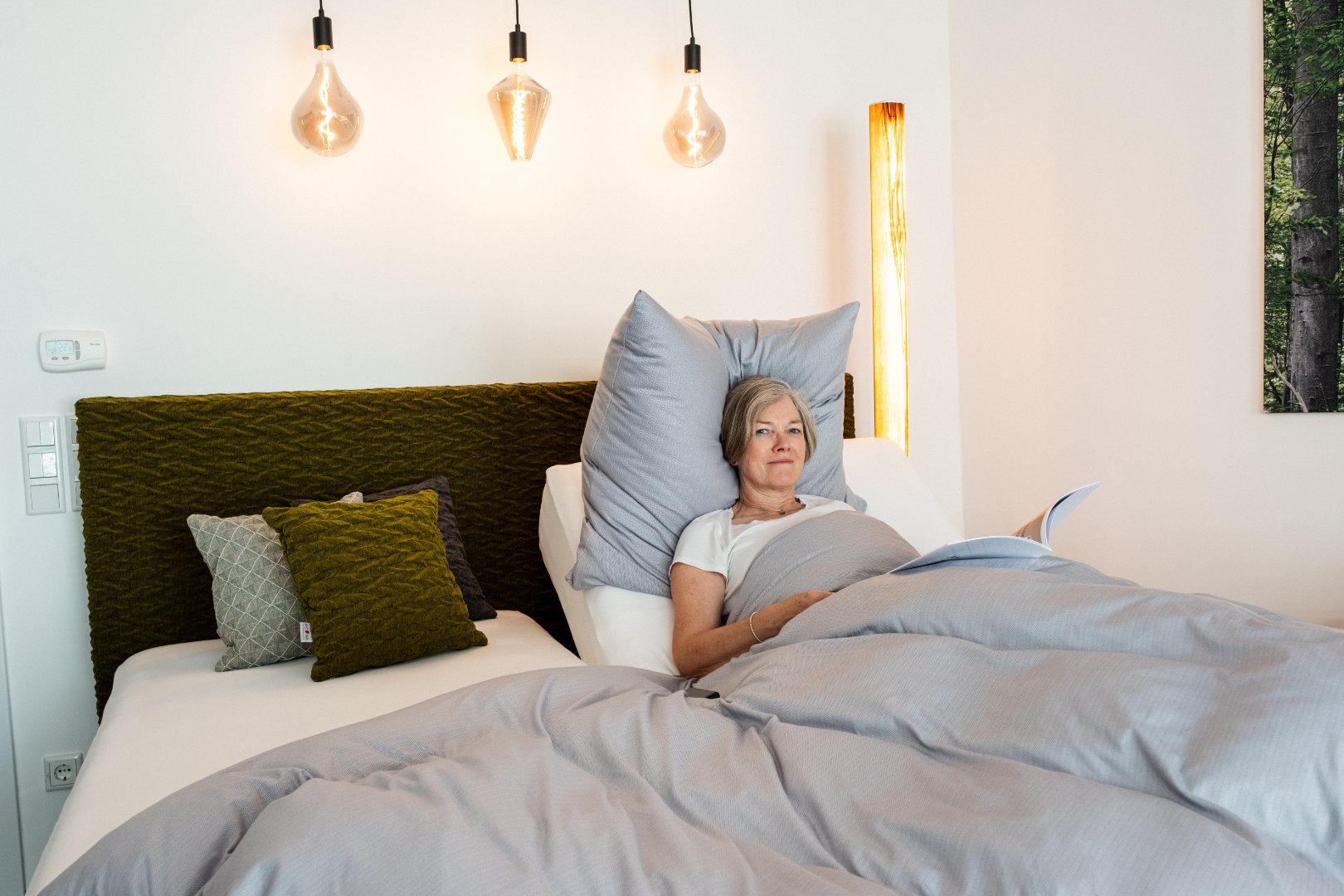 Eine Frau liegt entspannt in einem Bett mit grauen Kissen und einer Tagesdecke im Bettenfachgeschäft